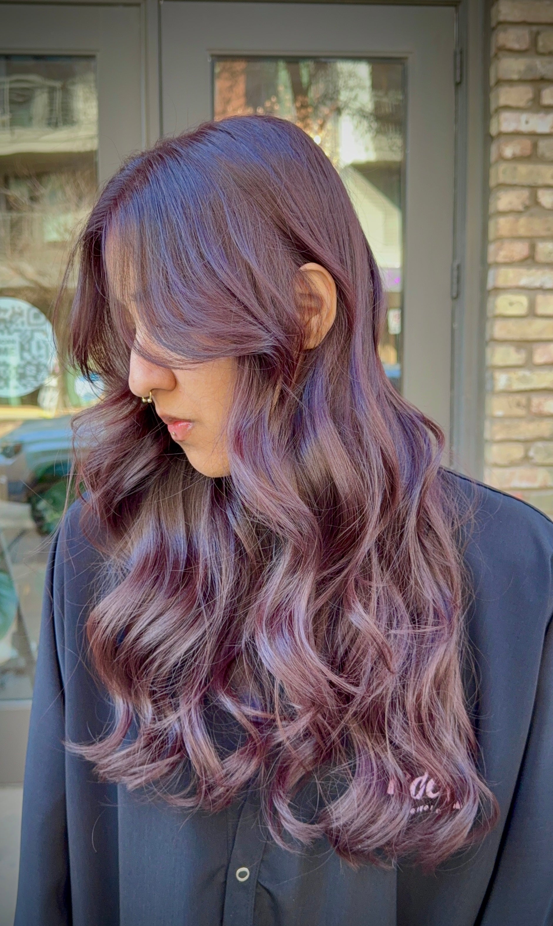 Person with wavy,  cherry cola hair standing outdoors.