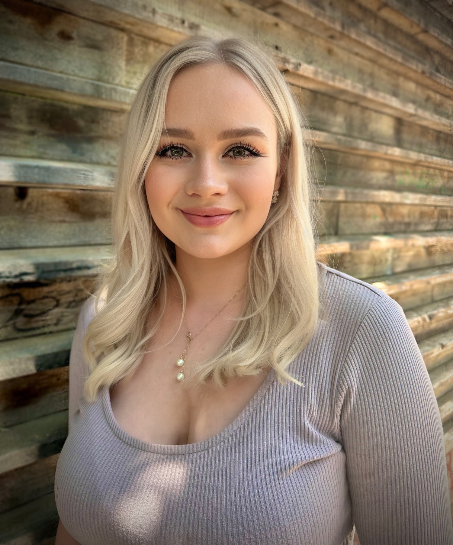 Woman with blonde hair standing in front of a wooden wall